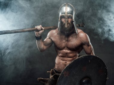 Zırhlı ve çıplak Viking dumanlı balta ve kalkanla poz veriyor.