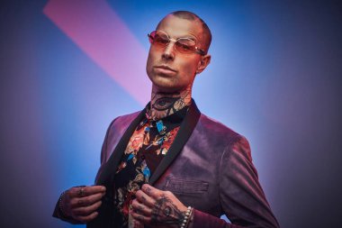 Özel ceketli, gözlüklü şık bir adam stüdyoda poz veriyor.