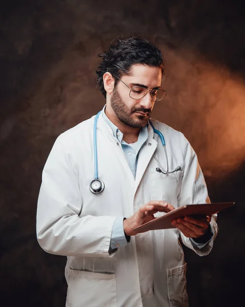 Mature doctor poses in dark background using his tablet — Stock Photo, Image