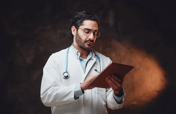 Mature médecin pose en arrière-plan sombre en utilisant sa tablette — Photo