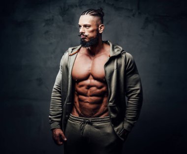 Gri spor kıyafetleri içinde çıplak gövdesi olan yakışıklı bir vücut geliştirici.
