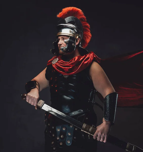 Legionary poses with sheathed sword in dark background — Stock Photo, Image