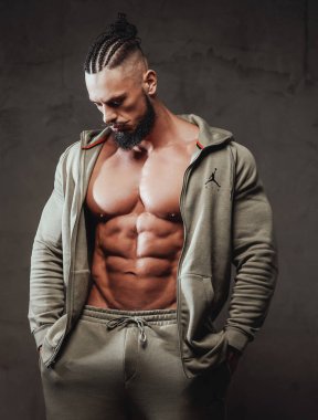 Gri spor kıyafetleri içinde çıplak gövdesi olan yakışıklı bir vücut geliştirici.