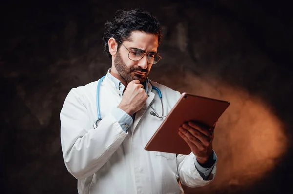 Médico pensativo en labcoat con tableta en fondo oscuro —  Fotos de Stock