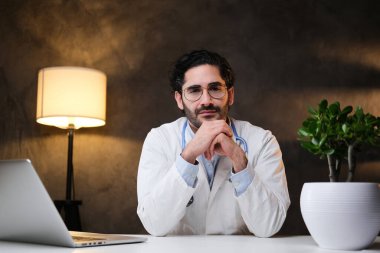 Cerrah masada oturur ve koyu arkaplanlı Camear 'a bakar