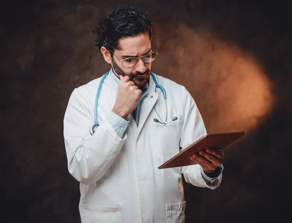 Pensive doctor in labcoat with tablet in dark background — Stock Photo, Image