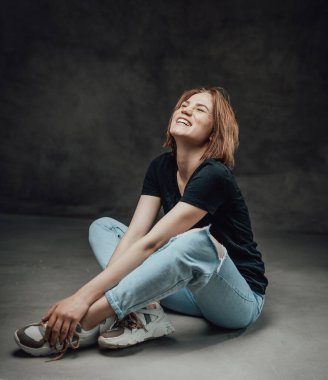 Kısa saçlı, kısa saçlı, esmer arka planda poz veren neşeli bir kız.