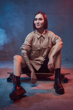 Güler yüzlü, kısa saçlı ve şık giyinmiş neşeli kız kaykayın üstünde dumanlı arka planda oturuyor..