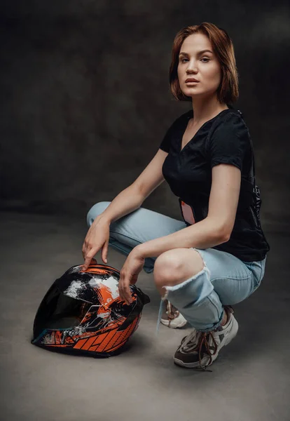 Femme motocycliste pose en arrière-plan sombre avec casque — Photo