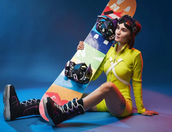 Veselá dívka se snowboardem pózuje v barevném pozadí — Stock fotografie