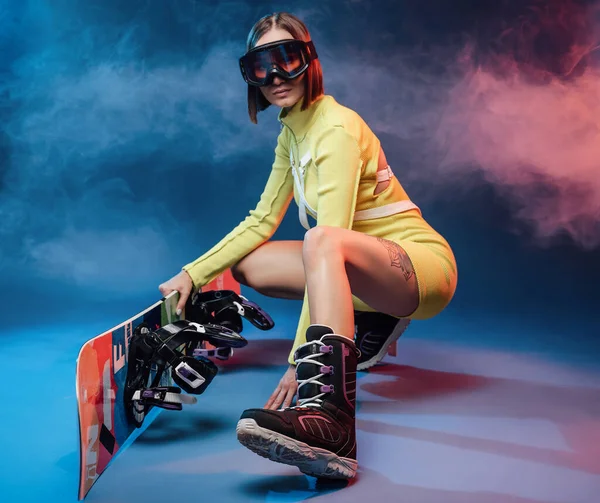 Chica alegre con snowboard en ropa deportiva amarilla en el estudio — Foto de Stock