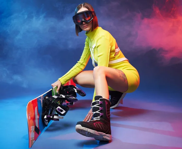 Ragazza carina con occhiali da sci e pose da snowboard in studio — Foto Stock