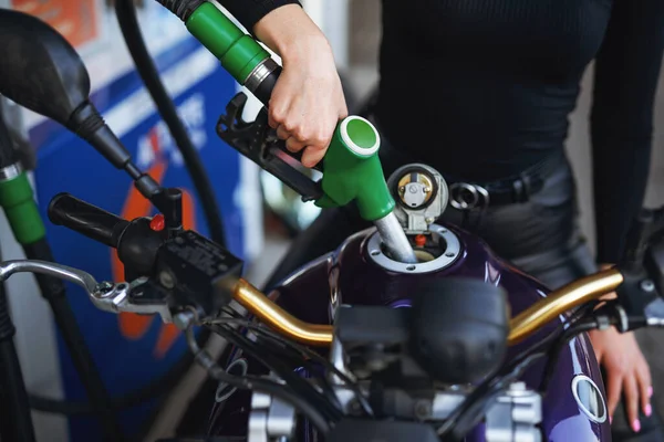 Een vrouw in donkere kleren vult haar motorfietsen tank — Stockfoto