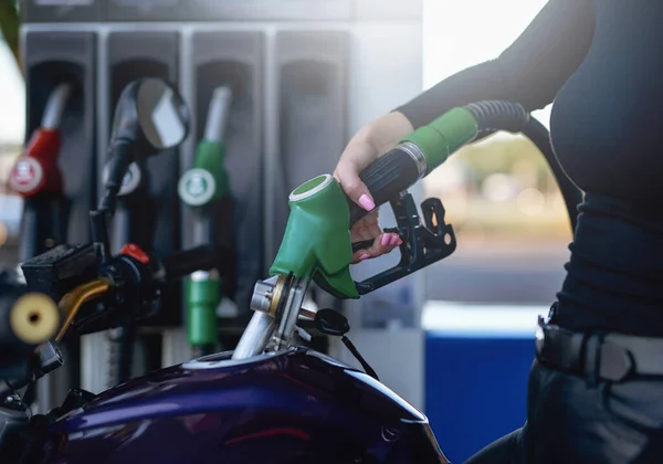 Een vrouw in donkere kleren vult haar motorfietsen tank — Stockfoto