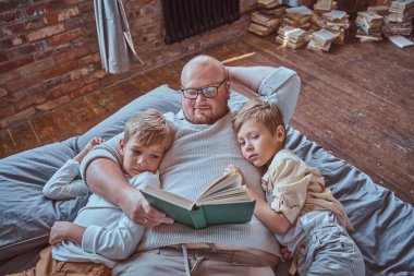 Baba ve iki oğlu yatak odasındaki yatakta yatan bir kitap okuyor.