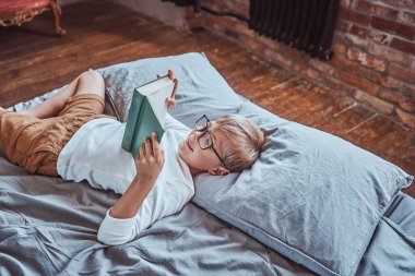 Neşeli anaokulu çocuğu kitap okuyor ve yatağa uzanıyor.