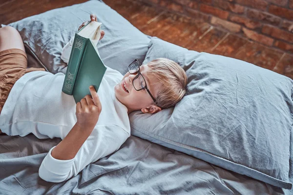 Pozitív fiú könyvet olvas a nappaliban fekszik az ágyon — Stock Fotó