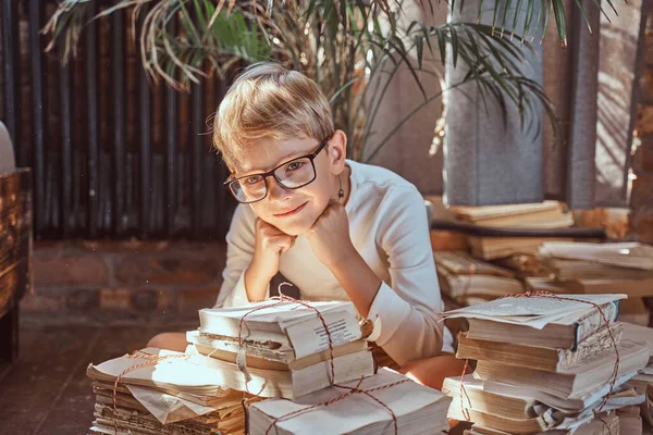 Positiv söt skolpojke sitter runt många böcker i rummet — Stockfoto
