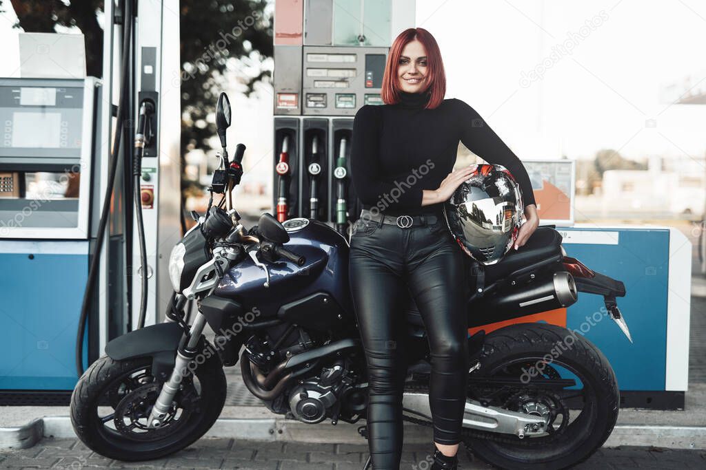 Smiling redhead woman with her custom bike in the gas station