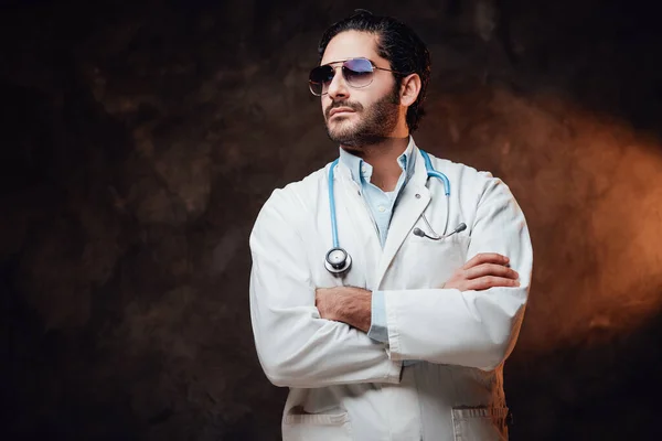 Brutális orvos pózol keresztbe tett karokkal sötét háttérben — Stock Fotó