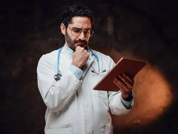 Médico serio de capa blanca sosteniendo el comprimido en fondo oscuro —  Fotos de Stock