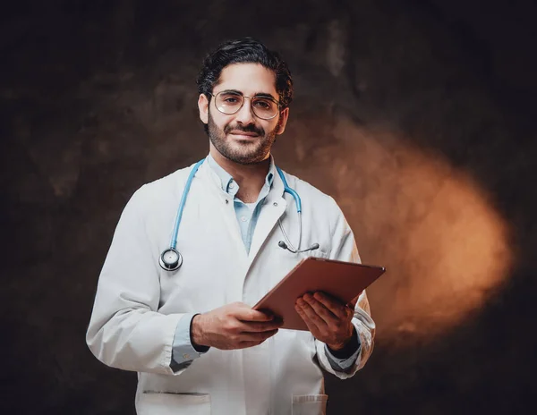Vidám orvos fehér kabátban tartó tabletta sötét háttérrel — Stock Fotó