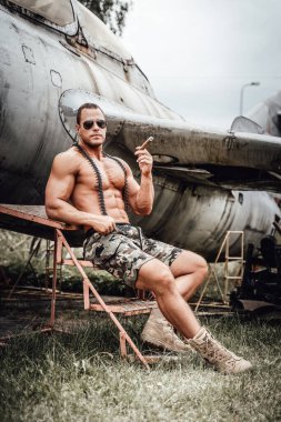 Acımasız Amerikan askeri elinde puroyla terk edilmiş uçağın yanında oturuyor.