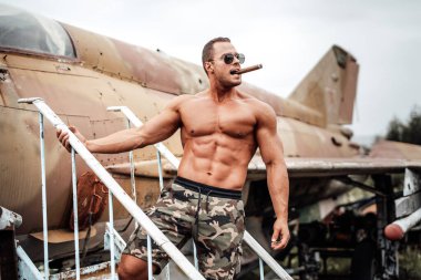 Güneş gözlüklü, puro içen kaslı üstsüz asker.