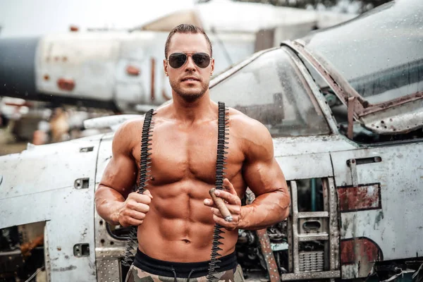 Topless bodybuilder with sunglasses and cigar near airplane — Stock Photo, Image