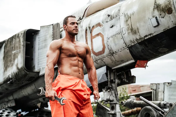 Segurando chaves muscular cara em roupas laranja perto de avião — Fotografia de Stock