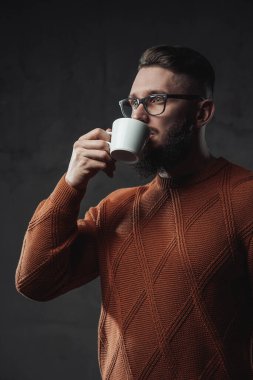 Ciddi sakallı adam koyu arkaplanda kahve içiyor.