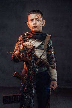 Siyah arka planda av tüfeği olan yırtık elbiseli bir çocuk.