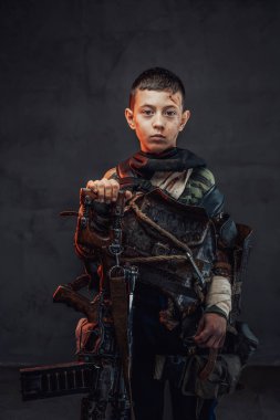 Siyah arka planda av tüfeği olan yırtık elbiseli bir çocuk.