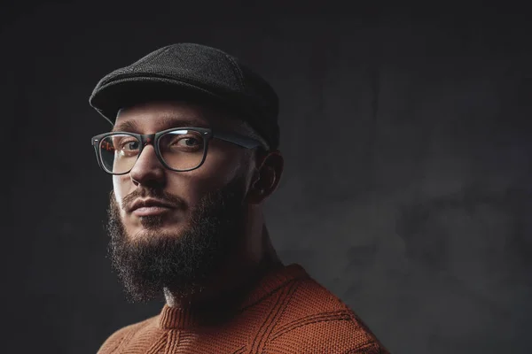 Serieuze hipster met baard en pet poserend in donkere achtergrond — Stockfoto