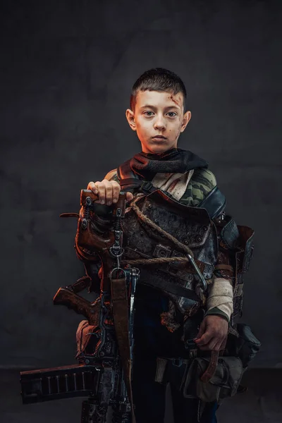 Young boy in ragged clothing with shotgun in dark background — Stock Photo, Image