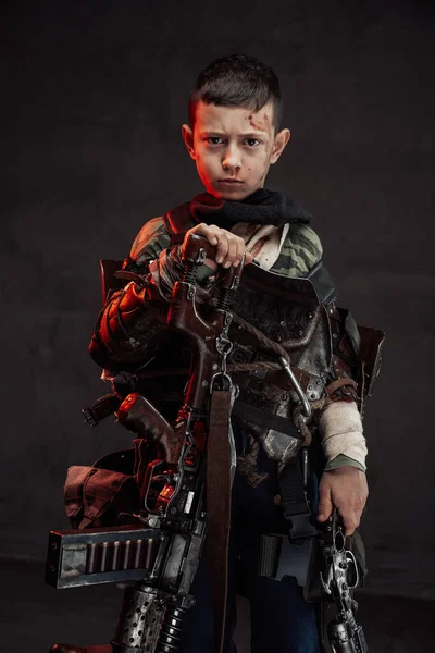 Young boy in ragged clothing with shotgun in dark background — Stock Photo, Image