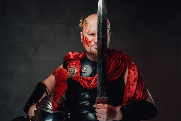 Roman guardian poses with sword near his face in dark background — Stock Photo, Image