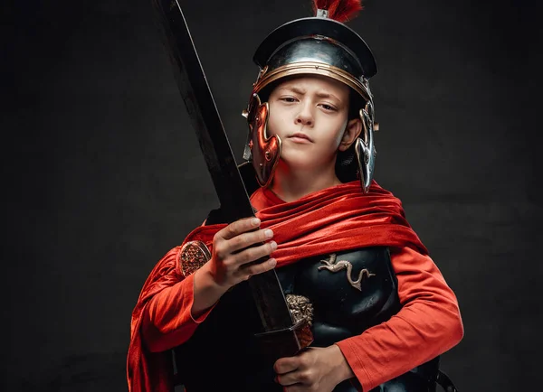 Cheerful roman boy with sword and red cape in dark background