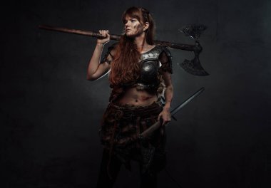 Ortaçağ dişi Viking savaşçısı, arka planda iki baltalı.