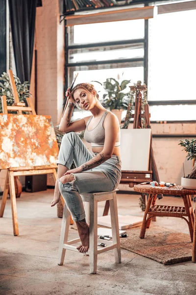 Glamour vrouwelijke schilder poseert zittend op stoel in haar werkruimte — Stockfoto