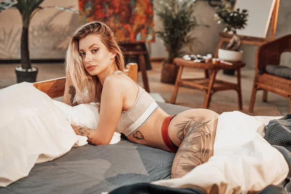 Seksualne wytatuowane kobieta stanowi leżąc na łóżku w studio — Zdjęcie stockowe