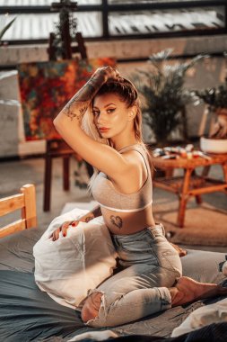 Rahat bir stüdyo odası ve yatakta yastıklı çekici bir kadın.