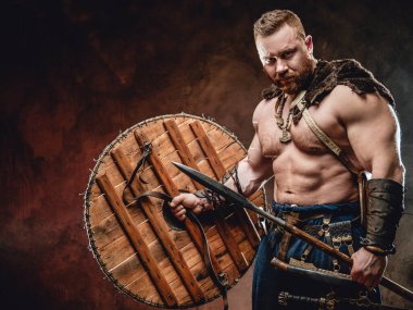Koyu kırmızı arka planda mızraklı yakışıklı Viking.