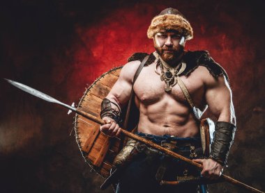 Koyu kırmızı arka planda mızrağı olan yakışıklı kuzeyli barbar.