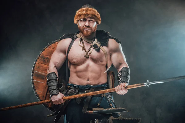 Vikingo sin camisa armado con lanza posa en un fondo ahumado — Foto de Stock