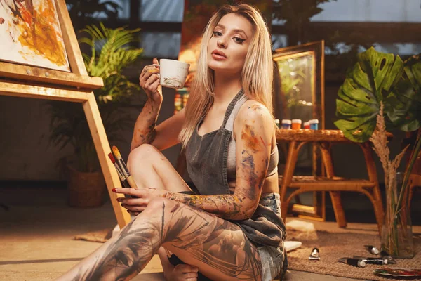 Förförisk grimmig blondin med kaffekopp i mörkt konstgalleri — Stockfoto