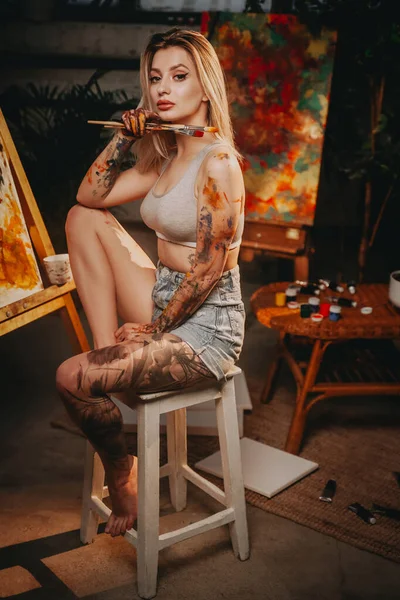 Stilvolle blondhaarige Frau sitzt auf Stuhl im dunklen Raum — Stockfoto