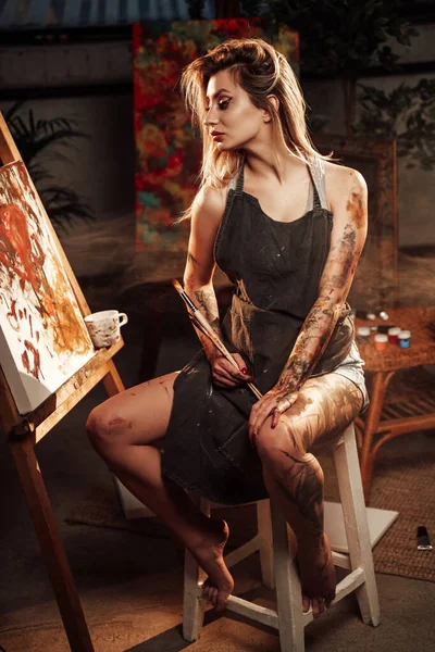 Artista donna con grembiule e pennelli vicino alla tela — Foto Stock
