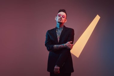 Siyah ceketli, renkli arka planda güneş gözlüklü modaya uygun bir hippi.