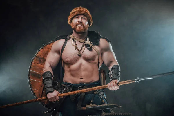 Karanlık ve dumanlı arka planda şapkası ve mızrağı olan gülen viking. — Stok fotoğraf